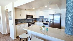 Cocina moderna con armarios blancos, una isla grande con taburetes de bar, electrodomésticos de acero inoxidable y un pilar decorativo azul.