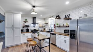 A modern kitchen with white cabinetry, a stainless steel refrigerator, and a wooden bar stool. - Pocono Retreat 4BR, Hot Tub,Game Room,  (Long Pond)
