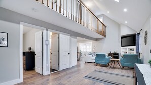 A spacious living area with a high ceiling, wooden flooring, and a balcony with a railing. - Pocono Retreat 4BR, Hot Tub,Game Room,  (Long Pond)
