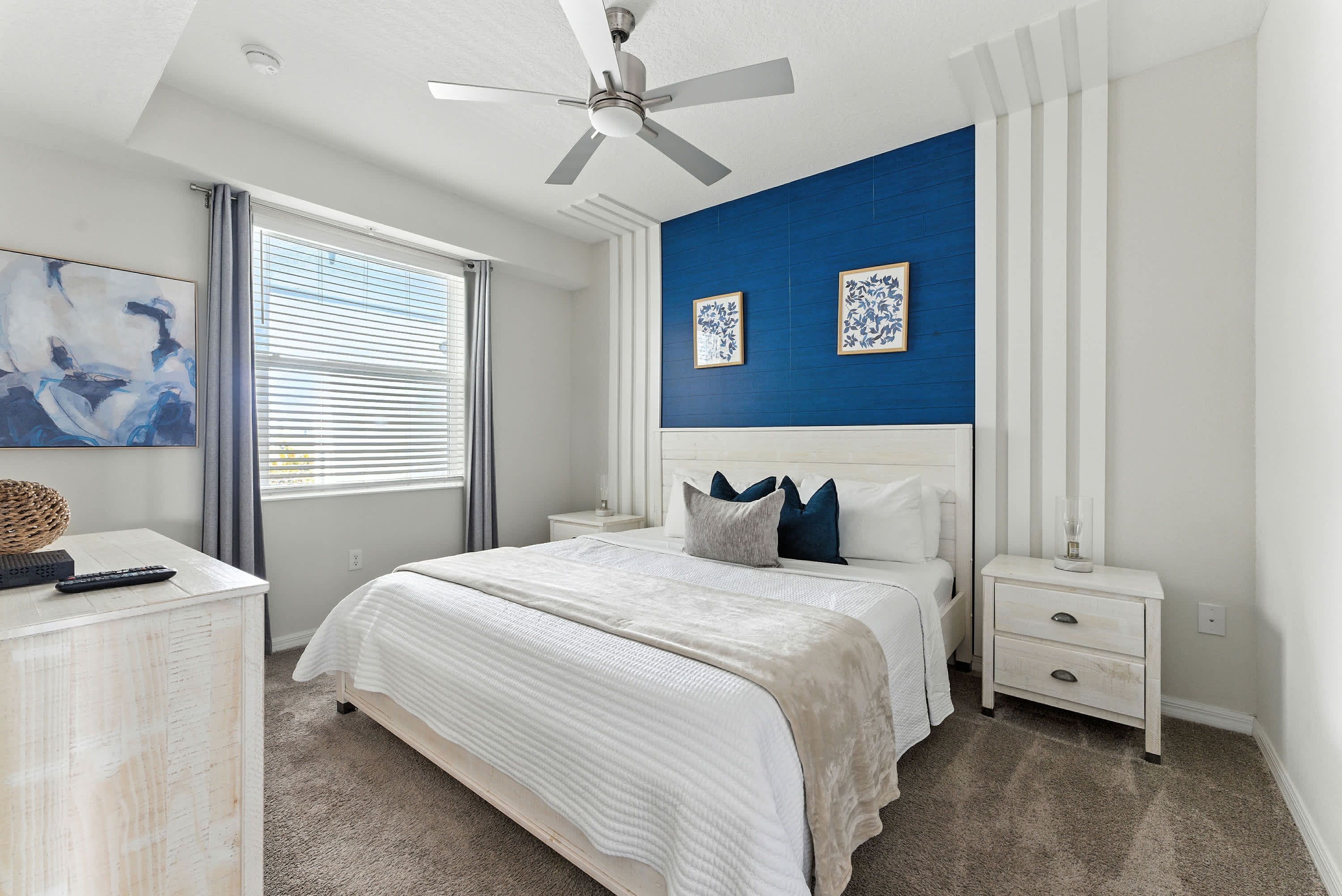 A bedroom with a bed, nightstands, a dresser, a ceiling fan, and artwork on the walls.