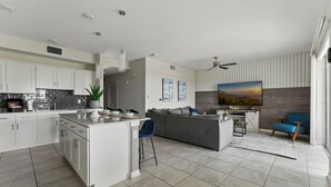 A modern kitchen with white cabinets, a central island, and a dining area with a blue chair. - Spacious 2BR Mickey Bedroom Lake View (Kissimmee)