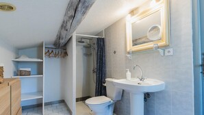 Een badkamer met toilet, wastafel en douche. Er is een handdoekhouder en een plank met een fles.