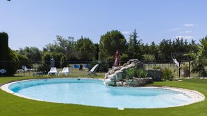 Une piscine agrémentée d’un élément rocheux, entourée d’une pelouse bien entretenue et d’une clôture.