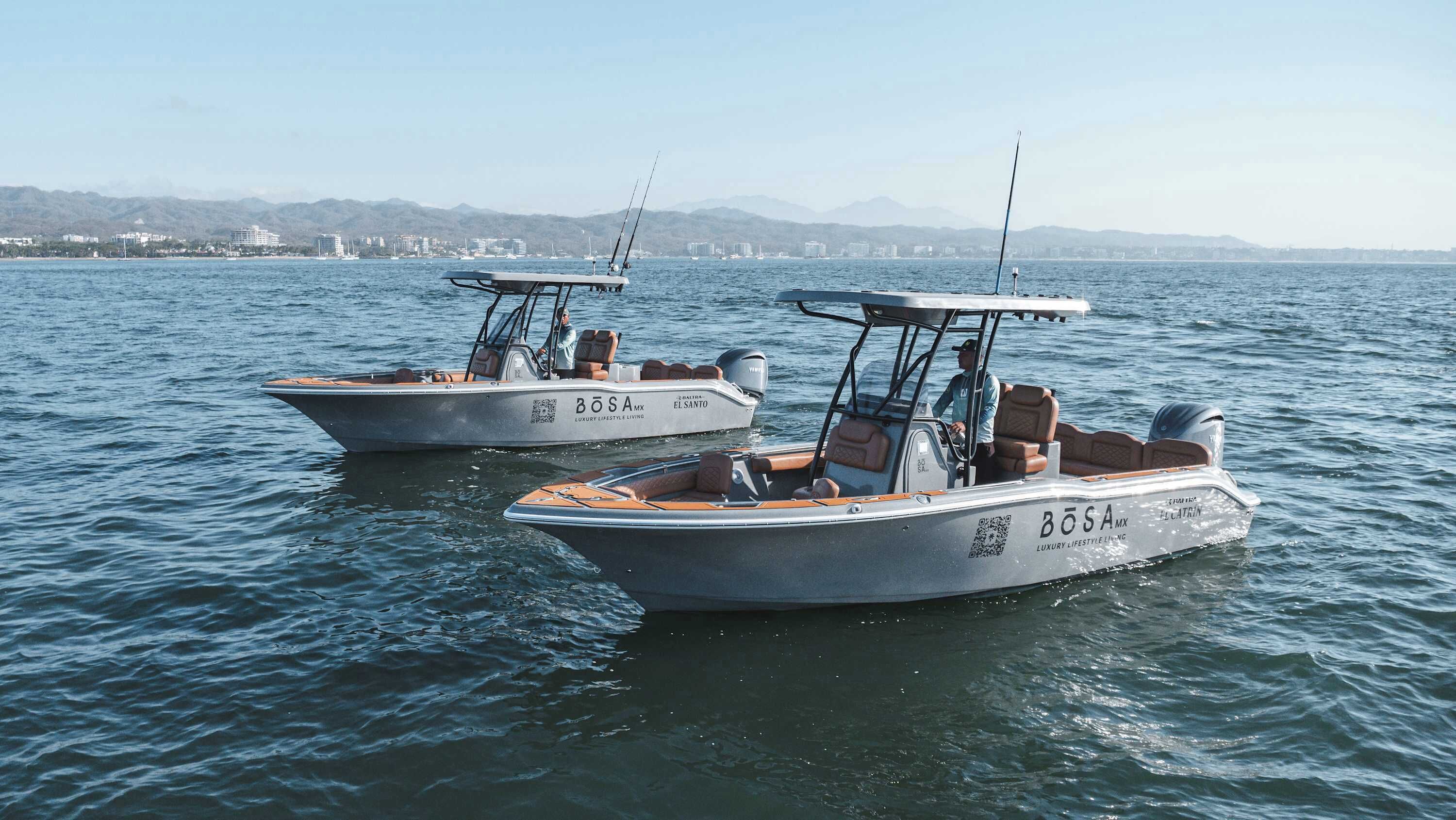 Two boats with 'BOSA MX' branding, equipped with seating and fishing rods, on calm water.