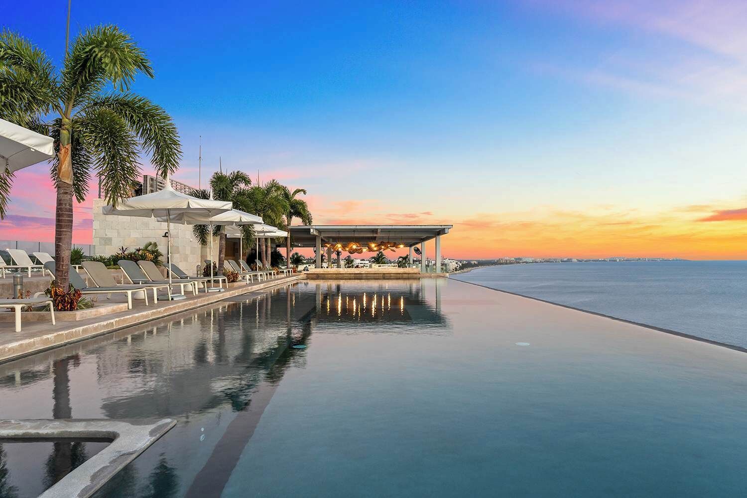 Ein Pool im Infinity-Stil mit Blick auf das Meer, Liegestühlen und Palmen.