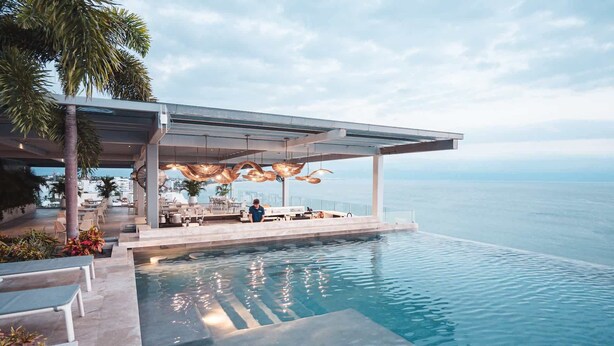 Ein luxuriöser Infinity-Pool mit freiem Blick auf den Ozean, eine überdachte Außenlounge mit modernen Möbeln und eine gepflegte Bepflanzung.