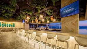 Eine Bar mit Korbstühlen und Tischen, einem Fernseher und Blick auf den Ozean.