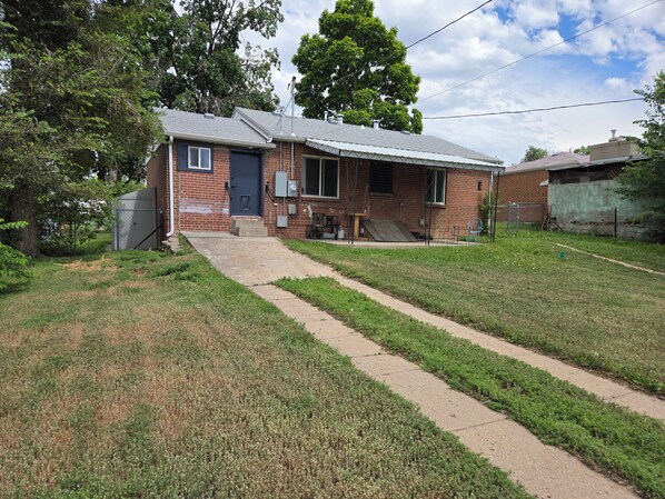 A single-story brick house with a front porch, a small attached garage, and a paved driveway leading to the entrance.