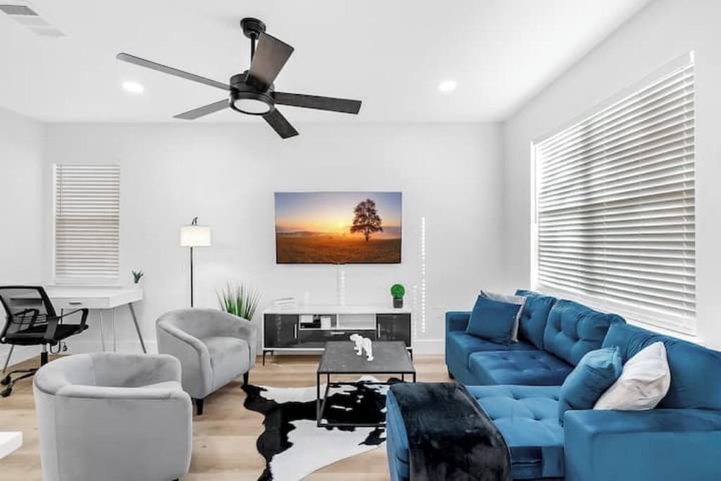 Een moderne woonkamer met een blauwe bank, een grijze fauteuil, een zwarte salontafel en een plafondventilator.