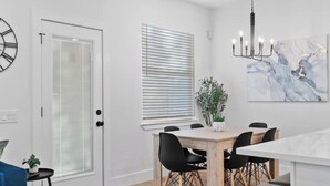 A modern dining area with a wooden table, black chairs, and a chandelier. - Comfy Blue ~ King & Queen Beds w/Fast Wi-Fi (Austin)