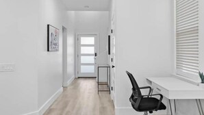 A modern, minimalistic hallway with a white desk and chair, a door at the end, and a framed picture on the wall. - Comfy Blue ~ King & Queen Beds w/Fast Wi-Fi (Austin)