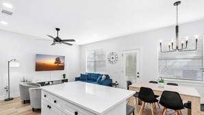 A modern living room with a white island, blue sofa, and a dining area with a table and chairs. - Comfy Blue ~ King & Queen Beds w/Fast Wi-Fi (Austin)