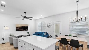 A modern living room with a white island, blue sofa, and a dining table with chairs. - Cozy & Spacious 2 Homes ~ Free Parking ~ 11 beds (Austin)