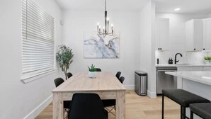 A modern kitchen with white cabinets, a wooden dining table, and a chandelier. - Cozy & Spacious 2 Homes ~ Free Parking ~ 11 beds (Austin)