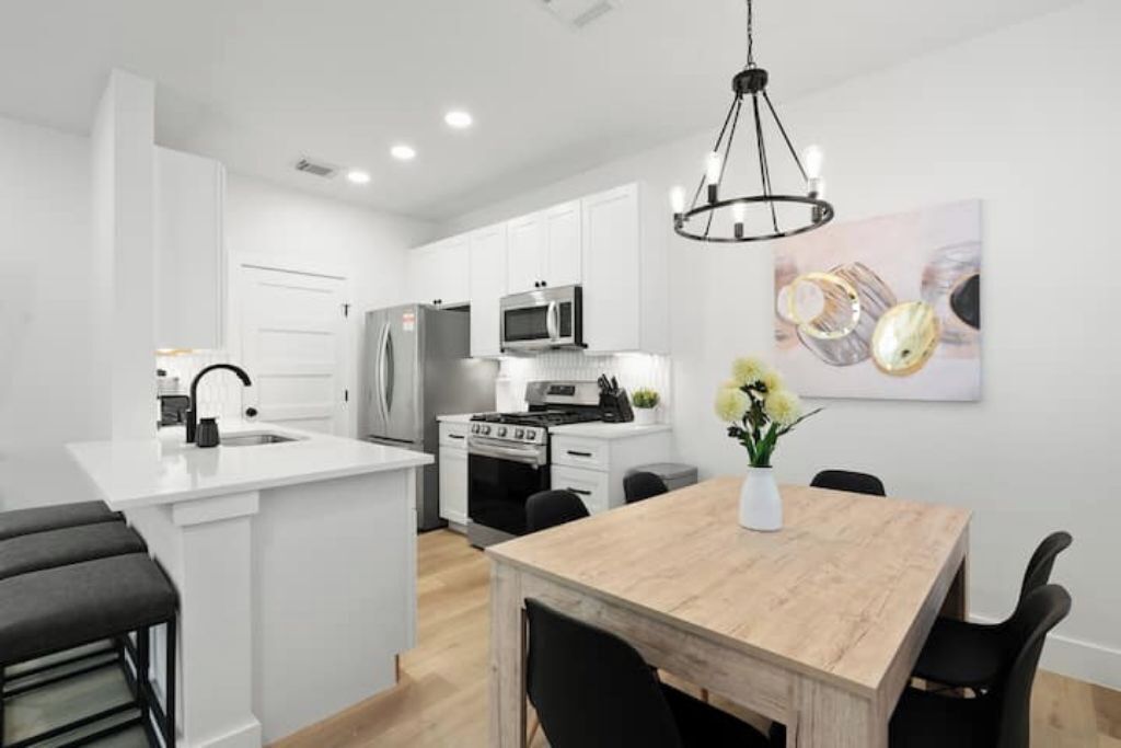 A modern kitchen with white cabinetry, stainless steel appliances, and a wooden dining table with black chairs.