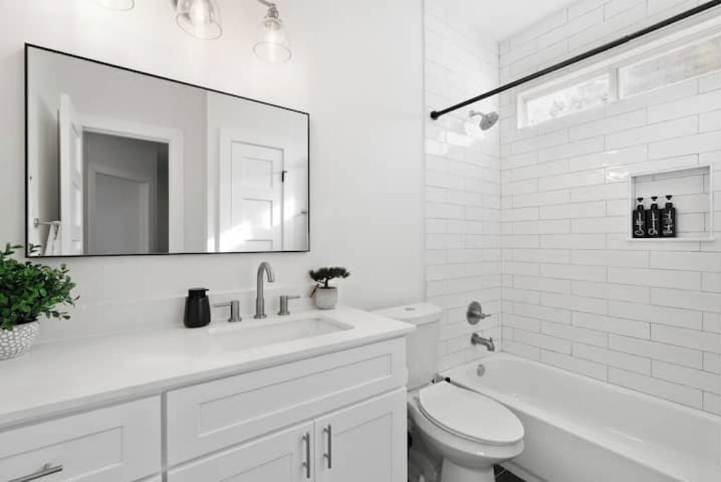 Casa de banho moderna com lavatório branco, espelho e sanita. Zona de duche com porta de vidro e pequena prateleira com artigos de higiene pessoal.