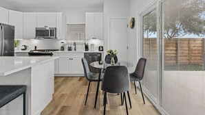 A modern kitchen with white cabinetry, a dining area with a round table and chairs, and a large window with a view of the outdoors. - ACL Ready ! ~ Near Downtown & Airport ~ Backyard! (Austin)