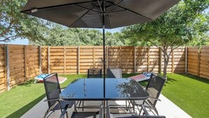 A patio with a table and chairs, an umbrella, and a wooden fence in the background. - ACL Ready ! ~ Near Downtown & Airport ~ Backyard! (Austin)