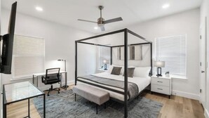 Een moderne slaapkamer met een hemelbed, een bureau en een stoel.