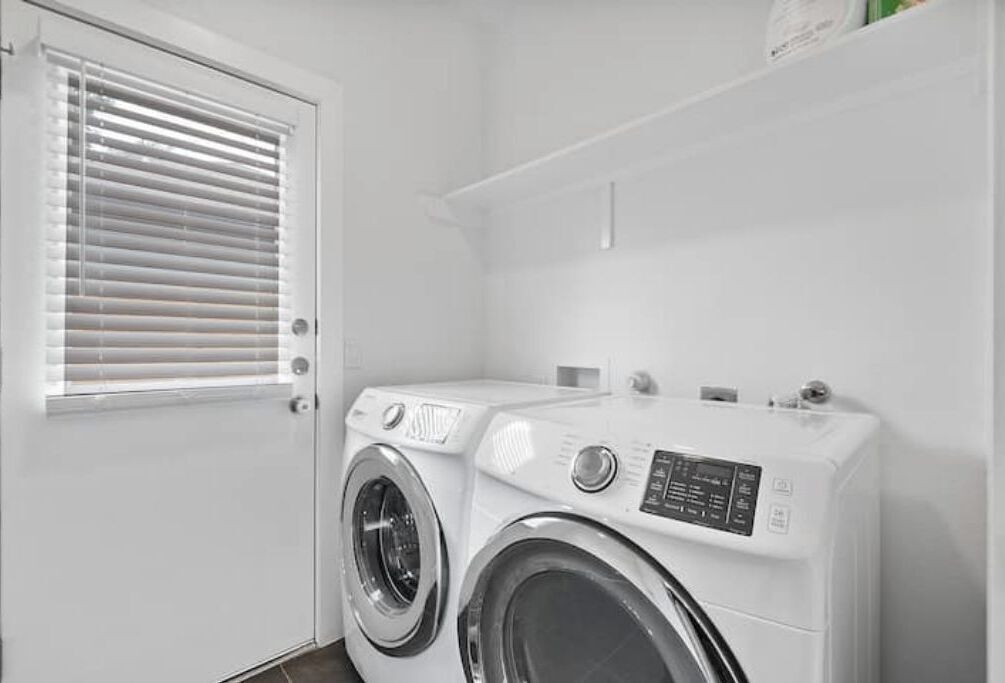 A compact laundry room with a front-loading washer and dryer, a door with a window, and a small shelf above the dryer.