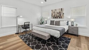 Une chambre à coucher comprenant un lit, des tables de chevet, un bureau, une chaise, un ventilateur de plafond et une fenêtre avec des stores.