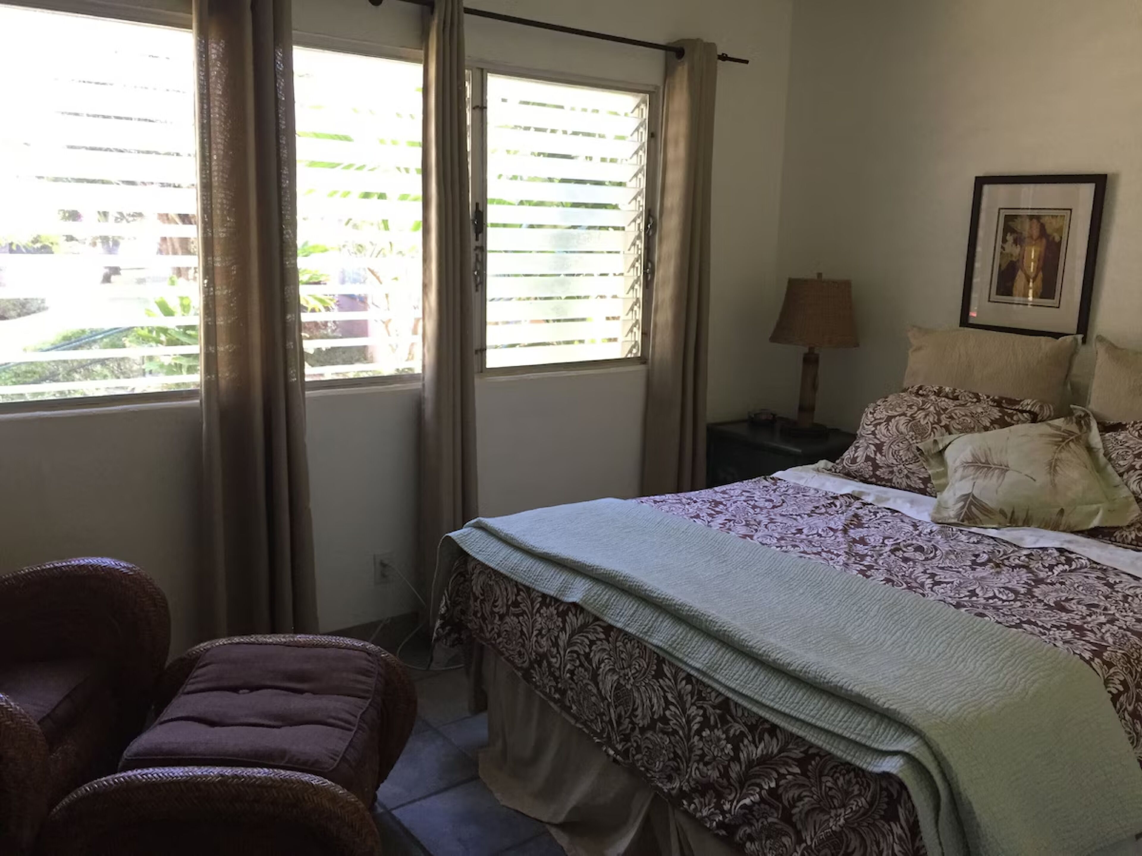 A bedroom with a bed, a nightstand, a lamp, a chair, and a window with blinds.