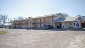 Un motel composé d’un bâtiment à deux étages, d’un espace de stationnement couvert et d’une allée en gravier.
