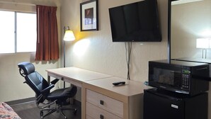 Une chambre d’hôtel avec un bureau en bois, une chaise de bureau noire, un téléviseur fixé au mur, un four à micro-ondes et un lit recouvert d’une courtepointe à motifs.