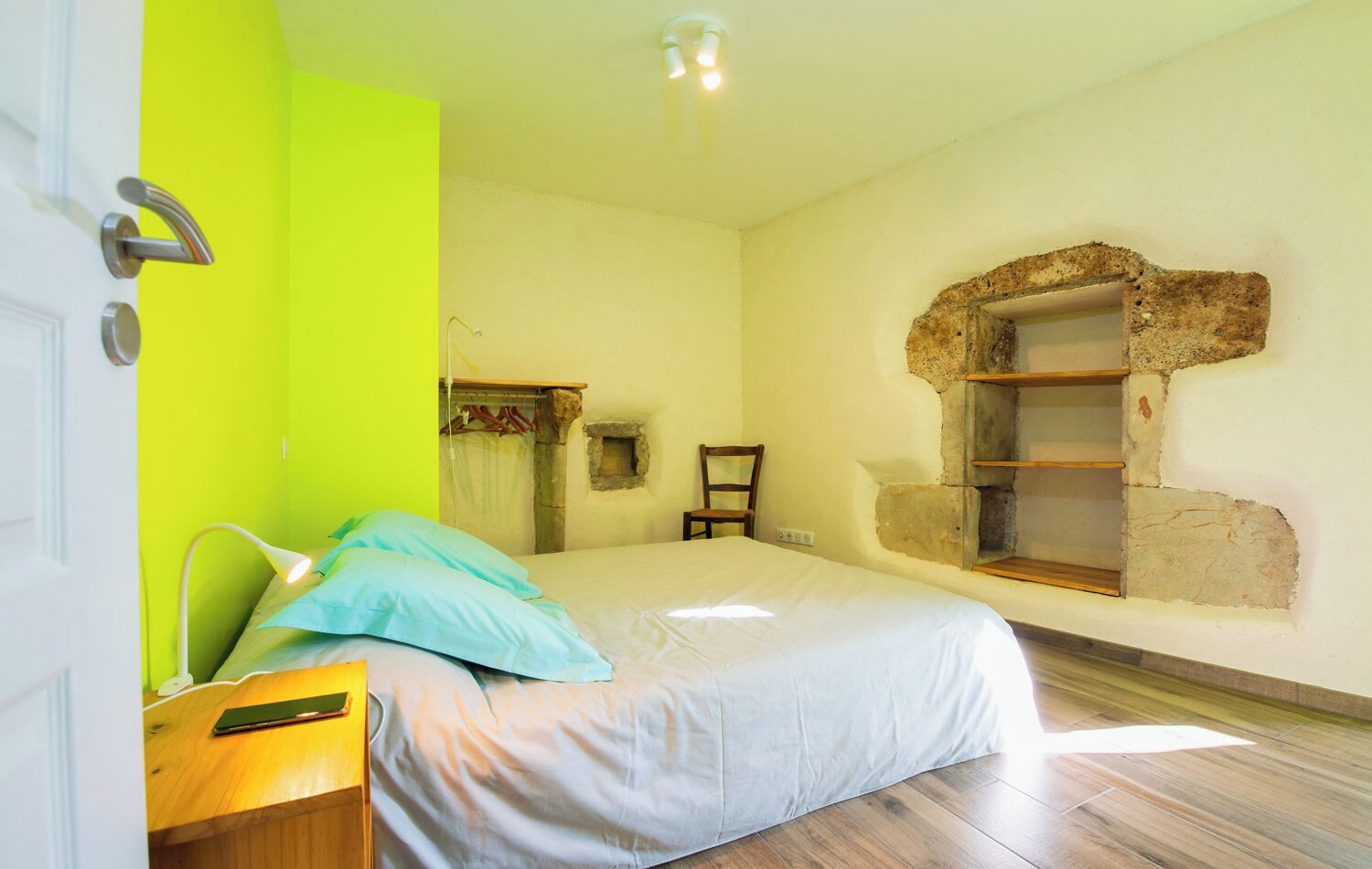 A bedroom with a bed, a nightstand, a chair, a window with a stone frame, and a bright green wall.