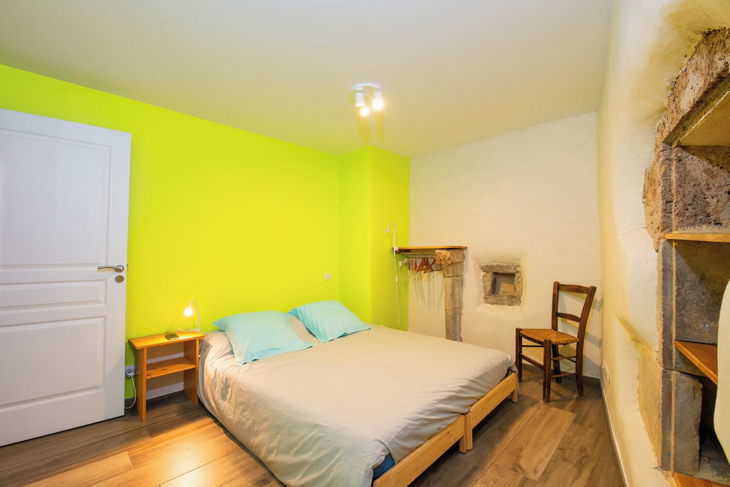 A room with a bed, a chair, a small table, and a wall-mounted shelf.
