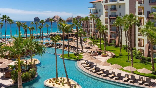 Un resort con varias piscinas, palmeras y vistas al océano.