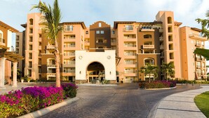 Un hotel de varios pisos con entrada central, balcones y jardines aledaños.
