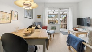A modern living room with a dining area, a TV, and a large window with a view. - Holiday bliss by forest and Bornholm’s top beach (Nexø)