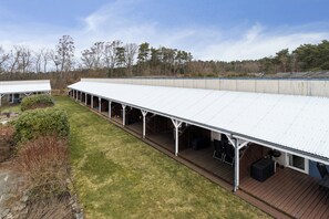 A covered outdoor area with a long, open-sided structure, a wooden deck, and a grassy lawn. - Holiday bliss by forest and Bornholm’s top beach (Nexø)