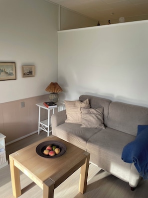 Ein Wohnzimmer mit einem beigen Sofa, einem kleinen weißen Tisch und einem Holztisch mit Obst.