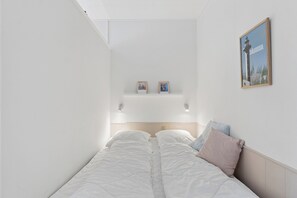 Ein Schlafzimmer mit einem Bett, einem Kopfteil, einem an der Wand montierten Regal mit zwei gerahmten Fotos und einem gerahmten Bild an der Wand.