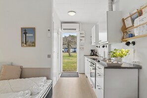 Een moderne hotelkamer met een bed, een kleine kitchenette, een deur naar een balkon en een lijst met een afbeelding aan de muur.