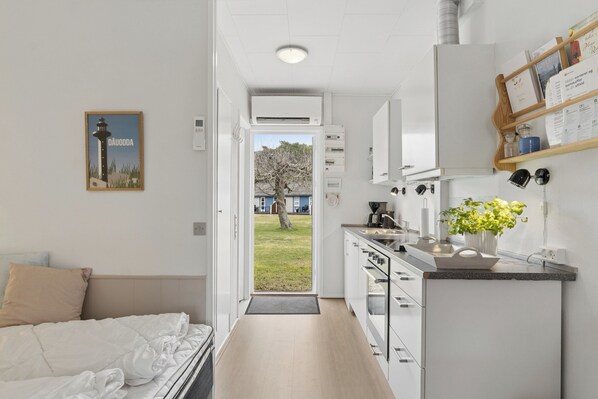 A modern hotel room with a bed, a small kitchenette, a door leading to a balcony, and a framed picture on the wall.