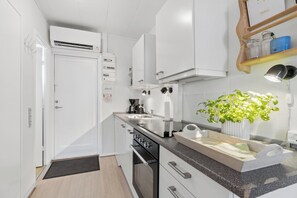 Een kleine keuken met witte kasten, een inbouwoven, een spoelbak en een aanrecht met een plant.
