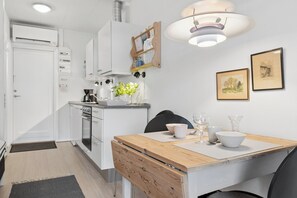 A modern kitchen with white cabinetry, a wooden dining table, and a hanging light fixture.