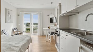 A modern hotel room with a bed, a dining area, a kitchen, and a balcony with a view. - Pension Koch, lejlighed 14 (Gudhjem)