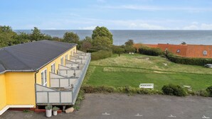 A yellow building with a black roof, a fenced area, and a view of the sea. - Pension Koch, lejlighed 14 (Gudhjem)