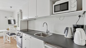 A modern kitchen with white cabinetry, a stainless steel sink, a microwave, a kettle, and a coffee maker. - Pension Koch, lejlighed 14 (Gudhjem)