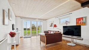 Ein modernes Wohnzimmer mit Holzboden, einer Ledersofa, einem Flachbildfernseher und einem großen Fenster.