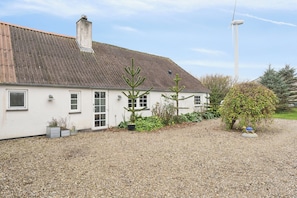 Un bâtiment blanc avec une allée de gravier, une cheminée et une éolienne en arrière-plan.