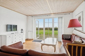 Un salon avec un téléviseur, des meubles blancs, un canapé en cuir marron, une table basse en bois et une lampe rouge.