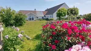 Ein Haus mit geneigtem Dach, einer Rasenfläche und verschiedenen blühenden Pflanzen.