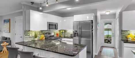 Cocina moderna con isla de granito, electrodomésticos de acero inoxidable y una zona de bar con taburetes.