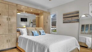 A bedroom with a large bed, wooden wardrobe, and a TV on the wall. - Beachside Bliss w/ Game Room, Gym & Golf Green (Westbrook)