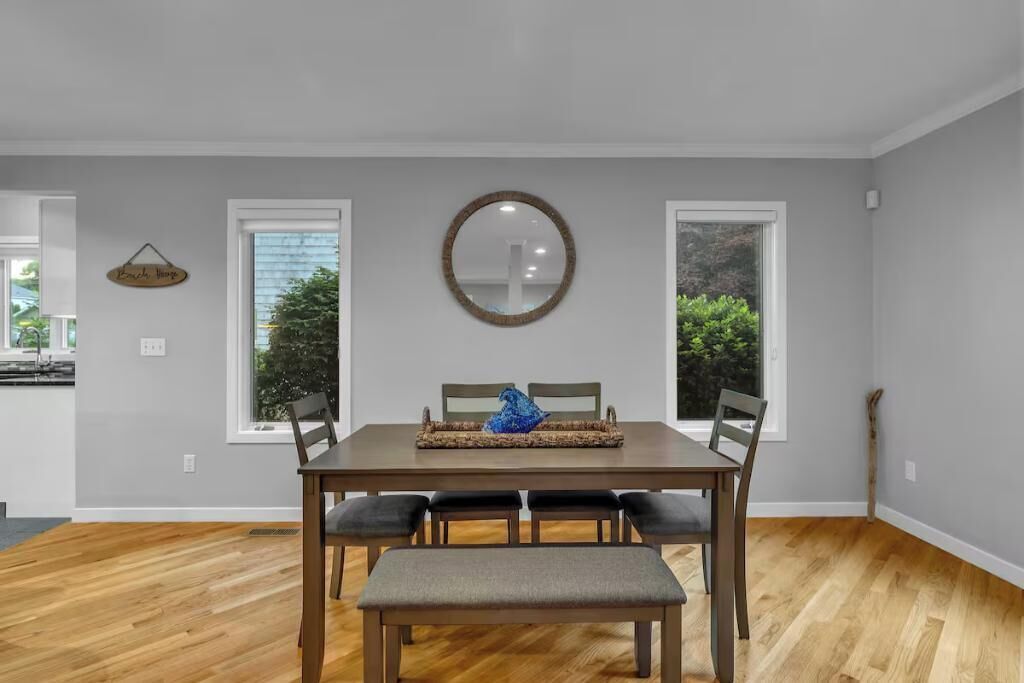 Un comedor con una mesa de madera, cuatro sillas y un banco. Hay dos ventanas con vistas a la vegetación exterior.